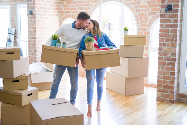 Young beautiful couple moving cardboard boxes and kissing at new home - Photo, Image