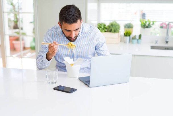 Üzleti ember eszik ázsiai ételeket a szállítási munka közben a számítógép laptop az irodában - Fotó, kép