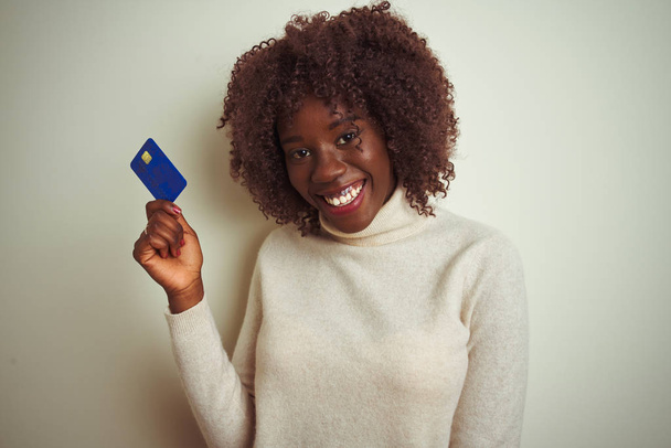 Young african afro woman holding credit card standing over isolated white background with a happy face standing and smiling with a confident smile showing teeth - Foto, Imagem