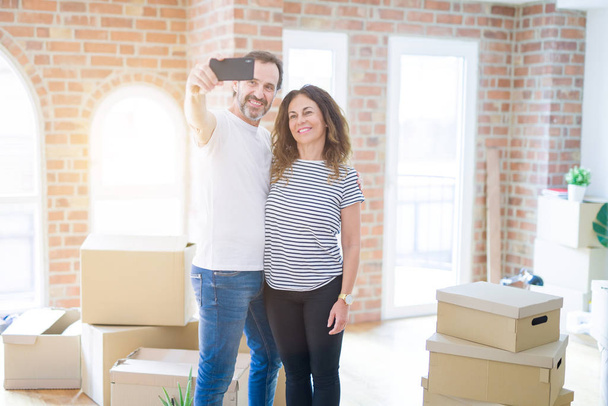 Middle age senior couple moving to a new house, holding cardboard boxing smiling happy in love with apartmant - Foto, immagini