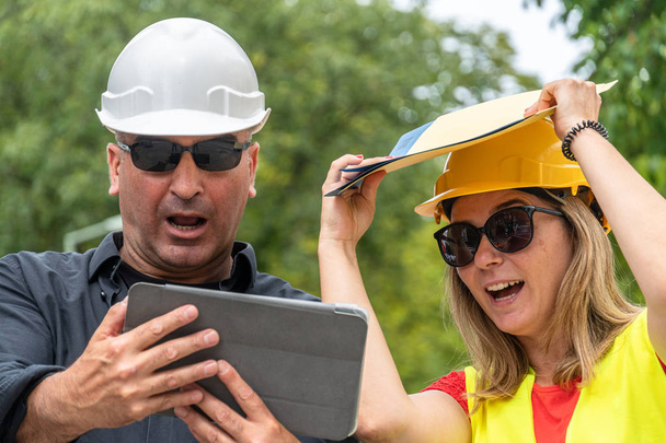 Work problem. Two scared, disappointed and surprised construction workers (male and female) reading bad news on the digital tablet - Photo, Image