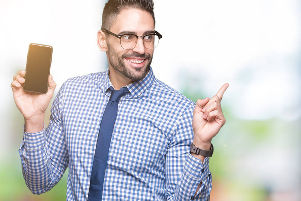 Joven hombre de negocios mostrando la pantalla del teléfono inteligente sobre un fondo aislado muy feliz apuntando con la mano y el dedo hacia un lado
 - Foto, Imagen