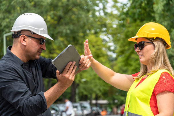 Conflict and disagreement at work on construction site. Angry construction boss yelling at an architect threatening to hit her with a digital tablet - Photo, Image