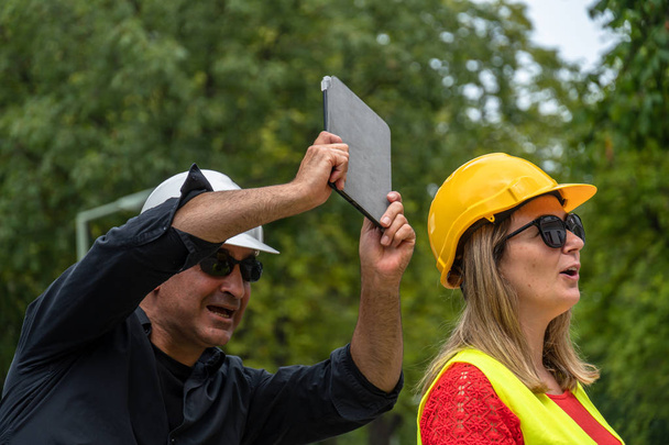 Conflict and disagreement at work on construction site. Angry construction boss yelling at an architect threatening to hit her with a digital tablet - Photo, Image