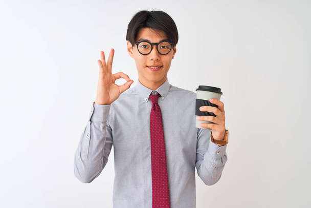 Chinese businessman wearing tie and glasses drinking coffee over isolated white background doing ok sign with fingers, excellent symbol - Foto, Imagen