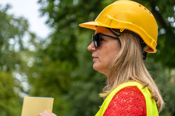 Close up profiel portret van een vrouw civiel ingenieur dragen gele beschermende helm en vest - Foto, afbeelding