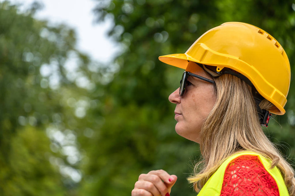 Close up profiel portret van een vrouw civiel ingenieur dragen gele beschermende helm en vest - Foto, afbeelding