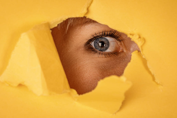 Mujer joven mirando a través de papel amarillo desgarrado
. - Foto, Imagen