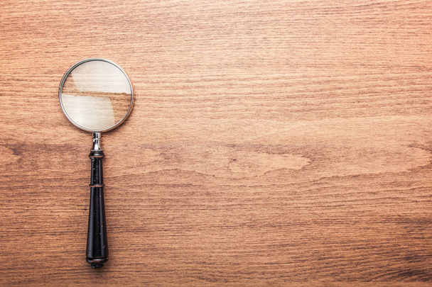 Magnifying glass on the dark brown wooden background - 写真・画像