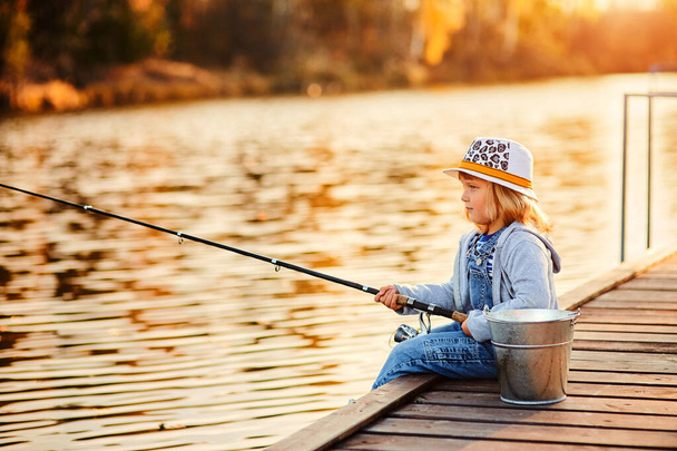 lonely little child fishing from wooden dock on lake. - Foto, afbeelding