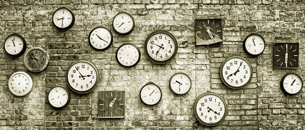 Uma coleção de relógios antigos diferentes de diferentes tempos no fundo de uma parede de tijolo velho com manchas e arranhões em tons preto e branco
 - Foto, Imagem