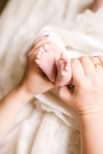 Мами і батька руки тримають маленькі милі ноги новонародженої дитини в домашніх умовах на білому ліжку. Щасливого материнства - Фото, зображення