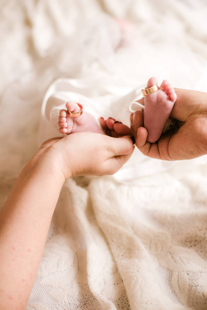 Mom's and father hands are holding little cute legs of a newborn baby at home on a white bed. Happy motherhood - Foto, Bild
