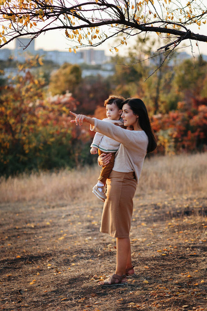 Young Caucasian mother with a boy child son baby in her hands walking and smiling in the autumn in nature - Photo, Image