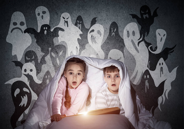 Scared girl and boy reading book in bed - Zdjęcie, obraz