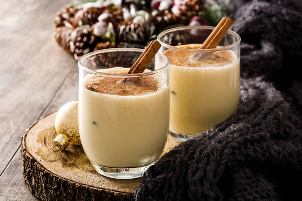 Homemade eggnog with cinnamon in glass on wooden table. Typical Christmas dessert.  - Фото, изображение