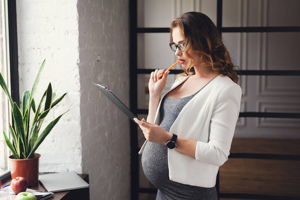 Беременная зрелая предпринимательница, работающая в офисе
 - Фото, изображение