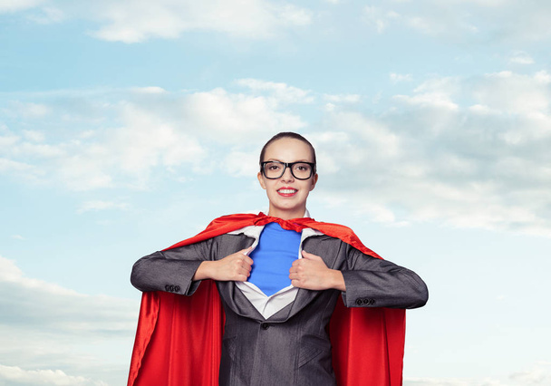 Portrait of business woman super heroine. Attractive young business lady in suit with red cloak on blue sky background. Successful and confident super woman in glasses ready for new challenges. - Photo, Image