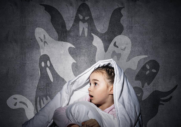 Scared girl with pillow hiding under blanket. Startled kid sitting in his bed at home. Little girl afraid of dark. Covered child not sleep at night. Fearful girl in pajamas and imaginary monsters. - Фото, изображение