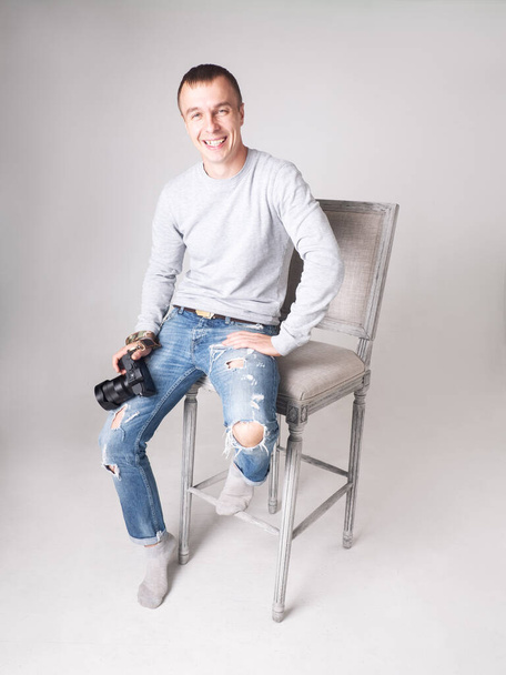 Een professionele fotograaf zit op een stoel in de studio en glimlacht oprecht. - Foto, afbeelding