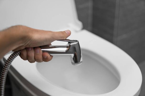 Using of bidet shower with a white toilet. Bidet shower in male hand for using with a white toilet bowl. - Foto, Imagem