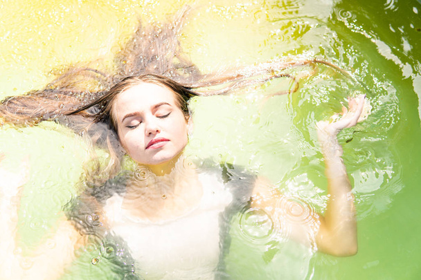 Krásná modelka oblečený v dlouhých večerních šatů, leží v bazénu a smyslně představuje - Fotografie, Obrázek