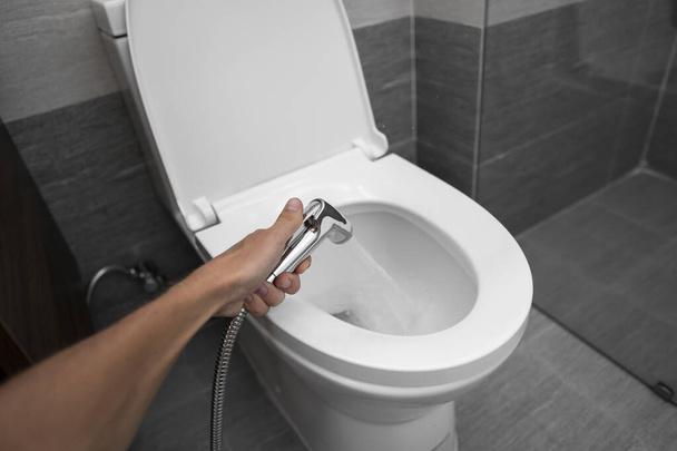Using of bidet shower with a white toilet. Bidet shower in male hand for using with a white toilet bowl. - Foto, afbeelding
