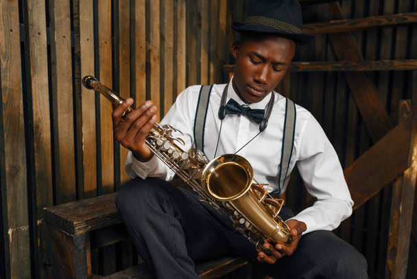 Afrikai jazz zenész, szaxofonos, fából készült fench háttérrel. Fekete jazzman kalapban pózol hangszeren - Fotó, kép