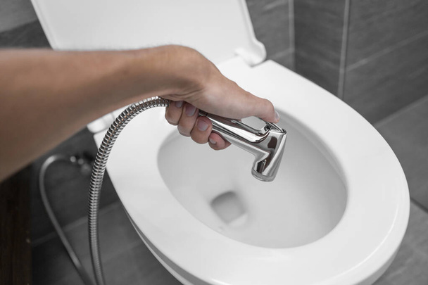 Using of bidet shower with a white toilet. Bidet shower in male hand for using with a white toilet bowl. - Foto, Bild