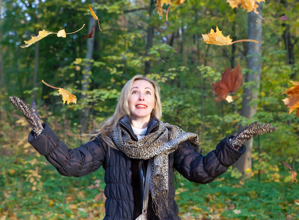 The beautiful woman in autumn park with an armful of maple leaves - Photo, Image