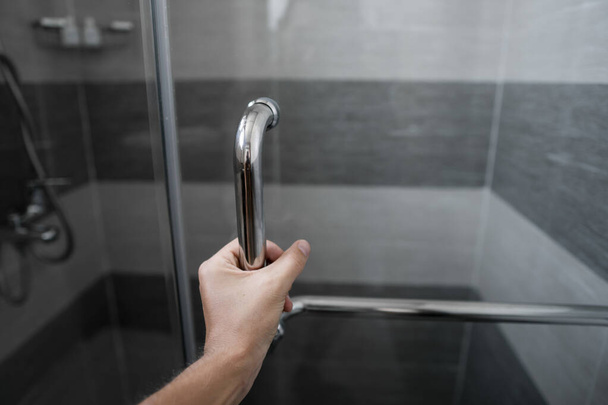Mano masculina abre la puerta de la ducha en un baño moderno
. - Foto, Imagen