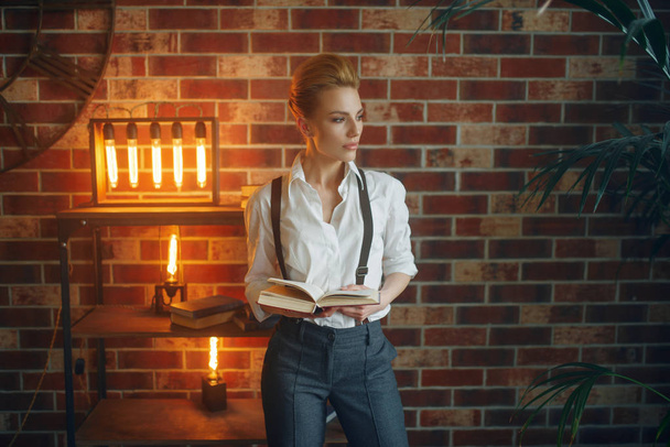 Business woman in strict clothes poses with book in studio, retro fashion, gangster style. Vintage lady in office with brick walls - Valokuva, kuva