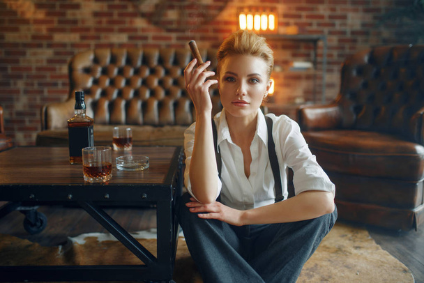 Business woman in strict clothes relax on the floor with whiskey and cigar, retro fashion, gangster style, female macho. Vintage lady in office with brick walls - Photo, Image