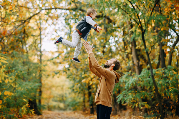 Father throws his son up while walking in the autumn forest. - Фото, изображение