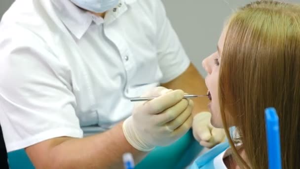 歯医者さん医者は鏡と特別な歯科器具で子供の歯を検査します。小児科の歯科医師室で小児患者が椅子に座っています。歯科治療の概念.4k - 映像、動画