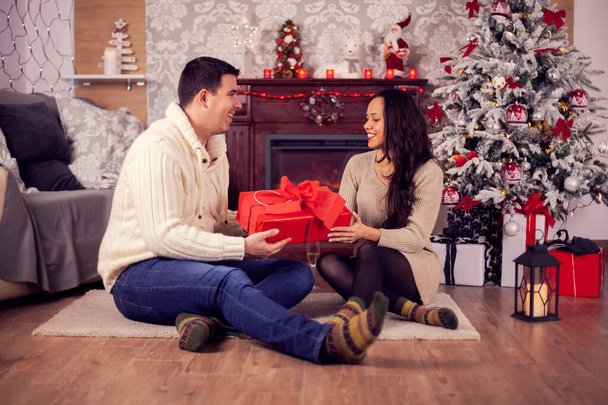 Romantic young couple sitting in front of a fireplace on christmas day - Фото, изображение
