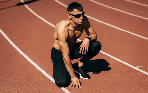 Shirtless fit man preparing for running on racetrack at stadium. Male runner sprinting during training session for competition. People, sport and healthy lifestyle - 写真・画像
