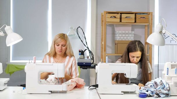 Couturières au travail en atelier vêtements à coudre sur machine à coudre, vue latérale
. - Photo, image