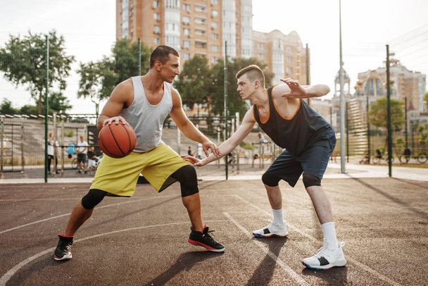 Dos jugadores en el centro del campo de baloncesto en la cancha al aire libre. Los atletas masculinos en ropa deportiva juegan el juego en el entrenamiento de streetball
 - Foto, imagen