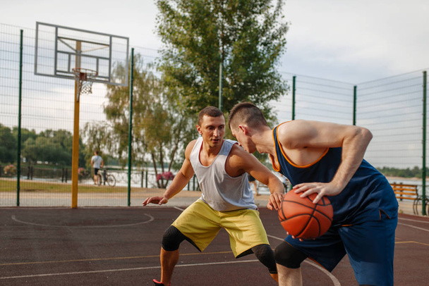 Δύο μπασκετμπολίστες παίζουν έντονο ματς σε υπαίθριο γήπεδο. Αρσενικοί αθλητές στα αθλητικά παίζουν το παιχνίδι στην προπόνηση streetball - Φωτογραφία, εικόνα