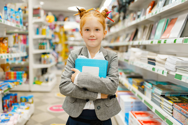 Μια μαθητριούλα με σημειωματάρια στο χαρτοπωλείο. Θηλυκό παιδί αγοράζει είδη γραφείου στο κατάστημα, σχολιαρόπαιδο στο σούπερ μάρκετ - Φωτογραφία, εικόνα