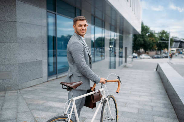 Un homme d'affaires en costume avec une mallette à vélo au centre-ville. Homme d'affaires à cheval sur l'éco transport sur la rue de la ville
 - Photo, image
