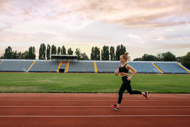 Жінка біжить у спортивному одязі, тренується на стадіоні. Жінка робить вправи, перш ніж бігати на відкритій арені
 - Фото, зображення