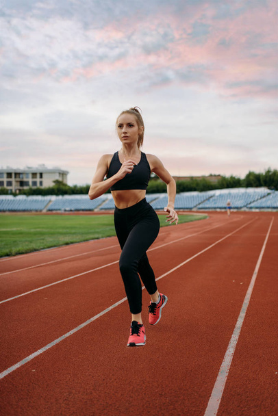 Бегунья в спортивной форме, тренировка на стадионе. Женщина делает упражнения на растяжку перед бегом на открытой арене
 - Фото, изображение