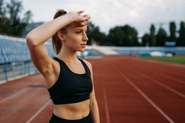 Tired female runner in sportswear, training on stadium. Woman doing stretching exercise before running on outdoor arena - Photo, Image