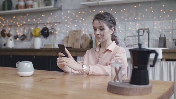 Young woman sitting at her kitchen table at home working on her small business with a smart phone. Stock footage. Portrait of a young lady tapping oh her mobile phone. - Photo, Image