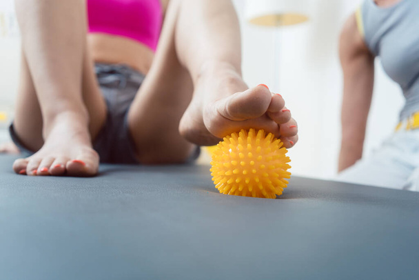 Mujer rodando bola de púas bajo sus pies en la terapia física - Foto, Imagen