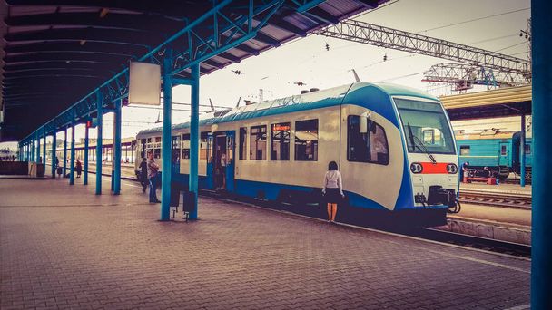 Bahnhof an einem bewölkten Sommertag. Der blaue Zug steht vor der Abfahrt. Schaffnerin und mehrere Fahrgäste stehen auf dem Bahnsteig. - Foto, Bild