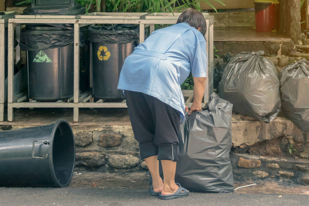 Kobieta pracownik sortowania śmieci i pakowane w czarne torby dla wygody transportu. - Zdjęcie, obraz