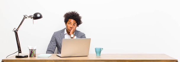 young black businessman feeling bored, frustrated and sleepy after a tiresome, dull and tedious task, holding face with hand on a desk - 写真・画像